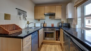 Una cocina moderna con armarios de madera, electrodomésticos de acero inoxidable, horno empotrado y un amplio ventanal.