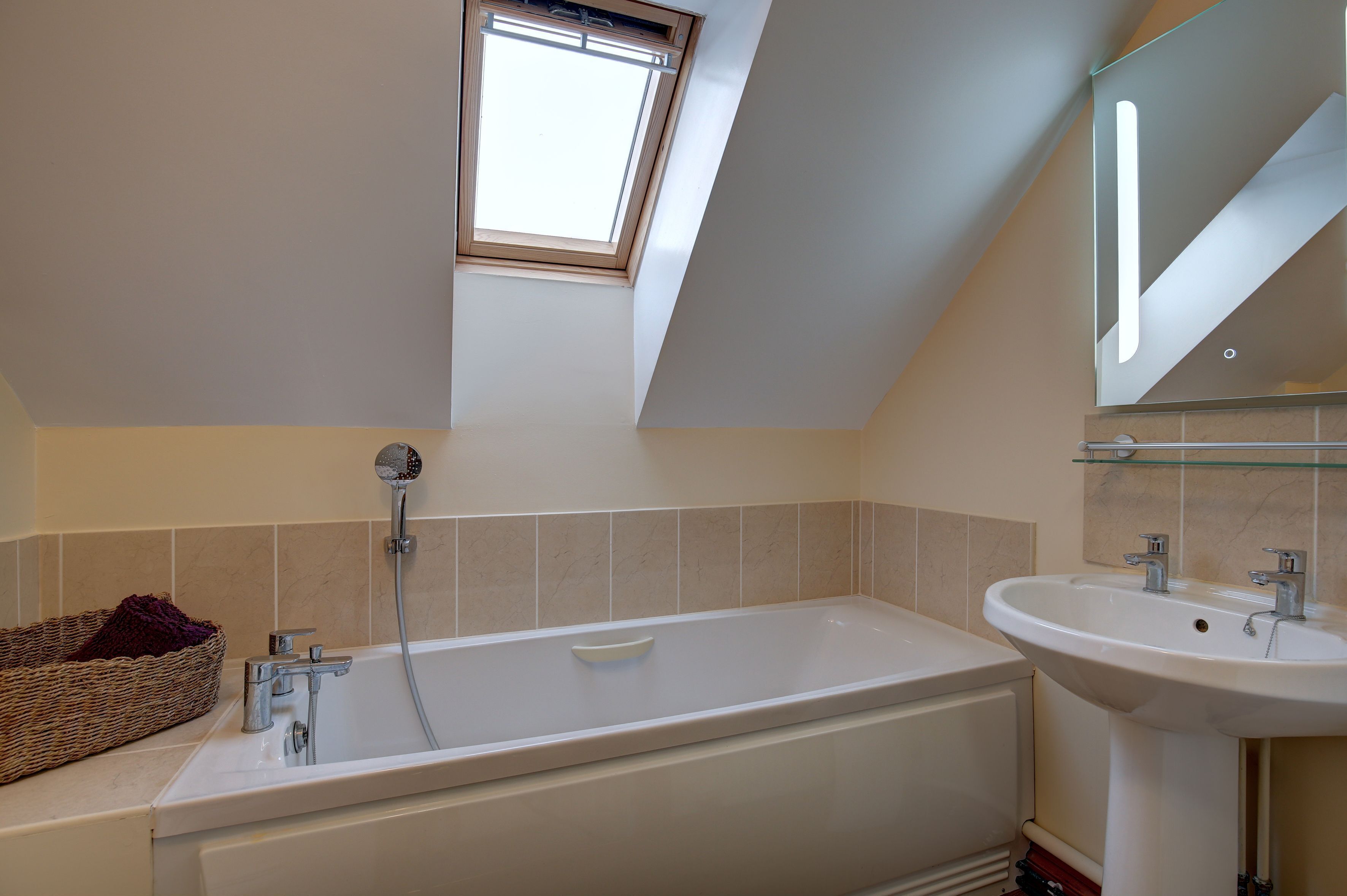 A bathroom with a skylight, a bathtub, a sink, and a wicker basket.