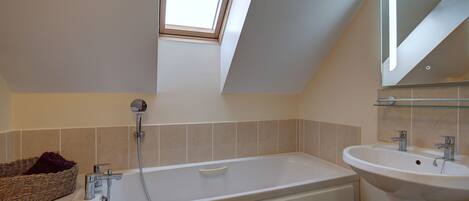 A bathroom with a skylight, a bathtub, a sink, and a wicker basket.