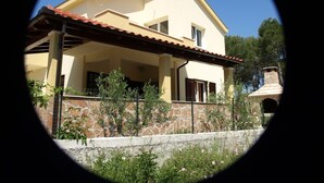 A two-story house with a covered patio, stone wall, and a chimney. - Apartments Mimose (Milna)