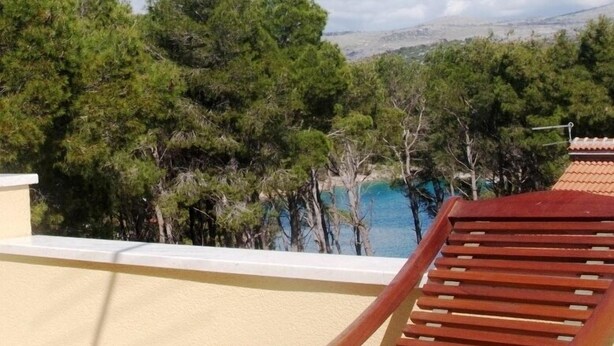 A wooden lounge chair on a balcony overlooking a coastal area with trees and a view of the sea. - Apartments Mimose (Milna)