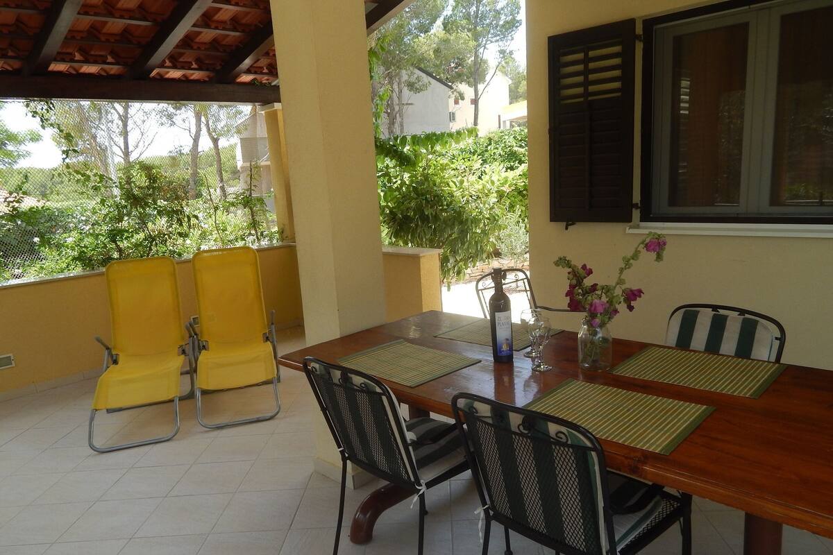 A covered patio with a wooden table, yellow chairs, and black mesh chairs.