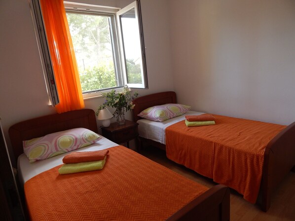A bedroom with two beds, each with an orange bedspread, a nightstand with a lamp, and a window with orange curtains.