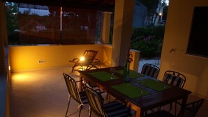 A covered patio with a wooden table and chairs, a vase with flowers, and a view of the outdoors. - Apartments Mimose (Milna)