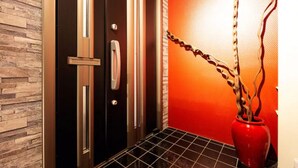 A modern elevator with a metallic finish, a red vase with branches, and a textured wall. - Ms Studio (Asahikawa)