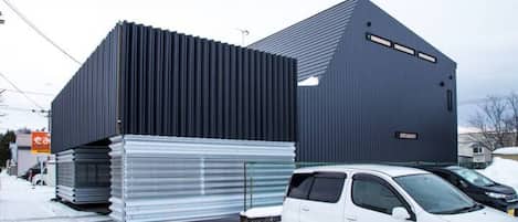 A modern building with a sloped roof and a large stack of metal sheets in front.