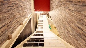 A narrow stairway with a red door at the top, flanked by textured stone walls. - Ms Studio (Asahikawa)