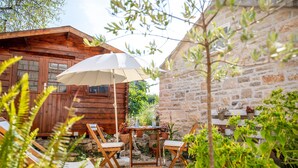 A wooden cabin with a stone wall, outdoor seating with a table and chairs, and potted plants. - Stone House Harmony (Korcula)