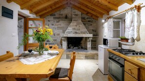 A rustic kitchen with a stone fireplace, wooden ceiling beams, and a dining table set with a vase of flowers and wine glasses. - Stone House Harmony (Korcula)