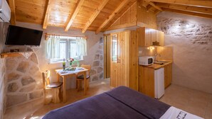 A cozy room with a bed, a wooden table with chairs, a small kitchen area, and a stone wall. - Stone House Harmony (Korcula)