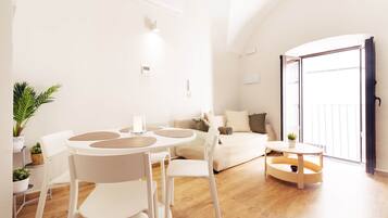 Ein modernes Wohnzimmer mit rundem Tisch, weißen Stühlen, einer Couch und einem Balkon.