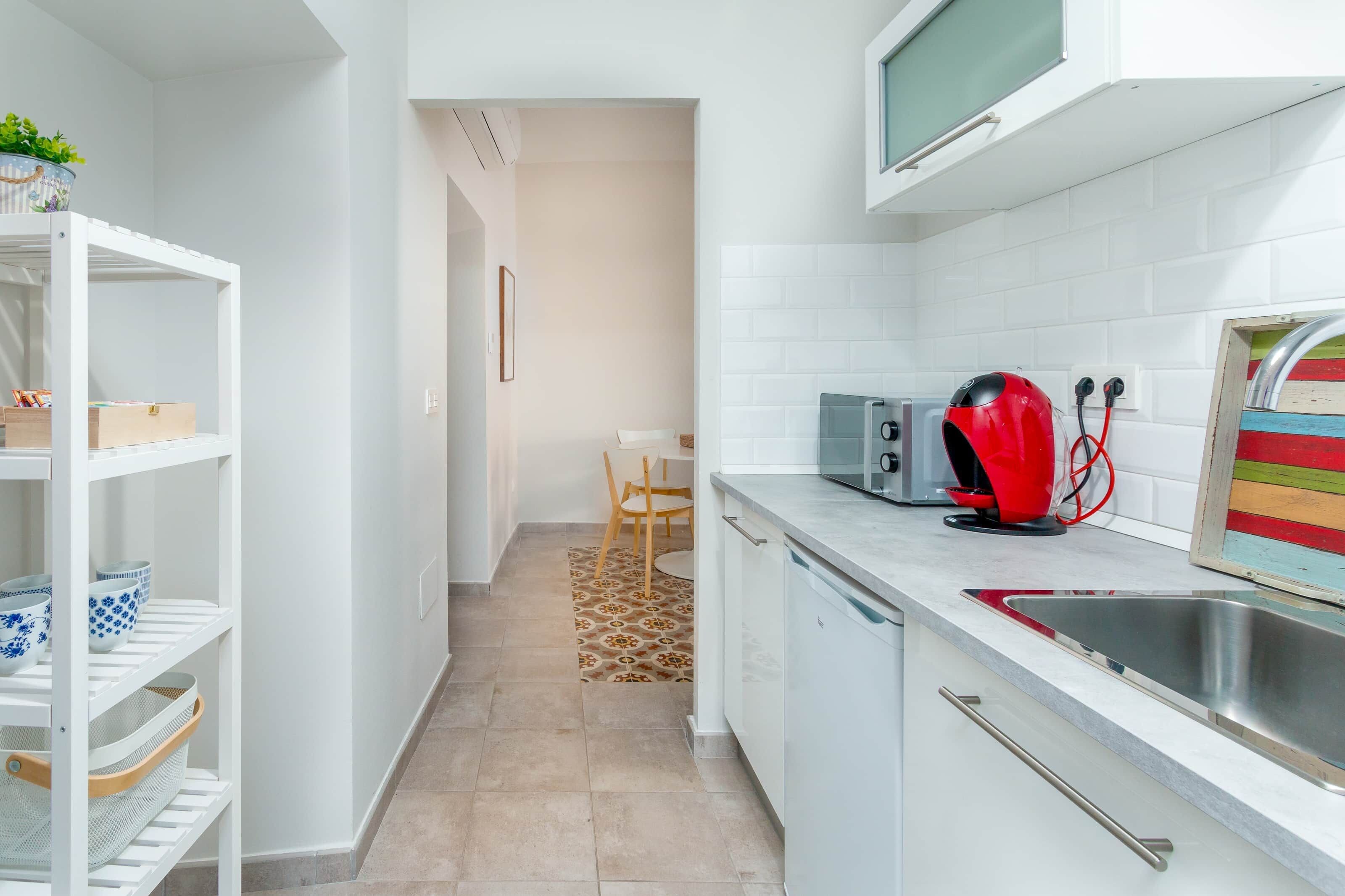 Una cocina moderna con armarios blancos, microondas, hervidor rojo y un mueble a rayas.