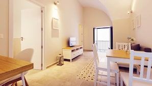 Un salon moderne comprenant un coin repas, un téléviseur posé sur un meuble blanc et un balcon doté d’une balustrade.