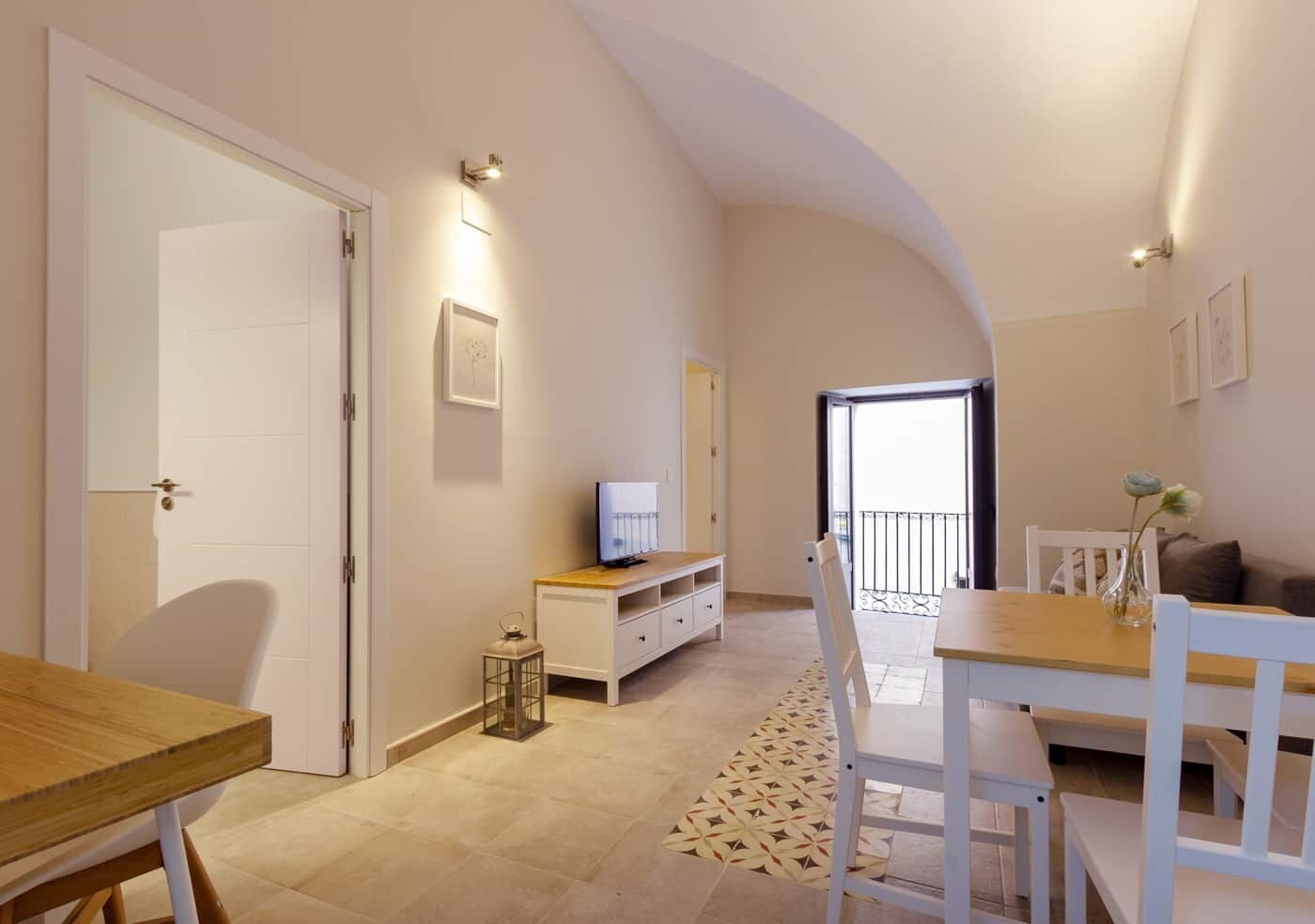 Un interior moderno con comedor, televisor sobre un mueble bajo y balcón con vistas.