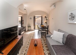A modern living room with a sofa, a coffee table, a TV, and a dining area with chairs and a table. - Apartments Plaza Mayor 35 (Cáceres‎)