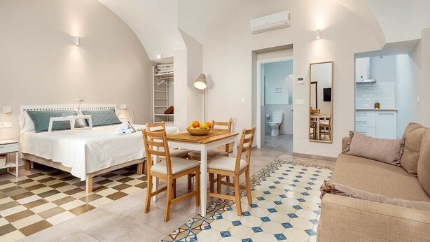 Une chambre avec un lit, une table de chevet et un petit bureau. On y trouve également un coin repas avec une table et des chaises, ainsi qu’une cuisine avec un comptoir et des placards.