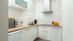 Une cuisine moderne avec des meubles blancs, un plan de travail en bois, un four à micro-ondes encastré, un évier et un panier à fruits.