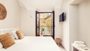 Ein Schlafzimmer mit einem großen Bett, einem an der Wand montierten Fernseher und einem Balkon mit Blick auf Gebäude.
