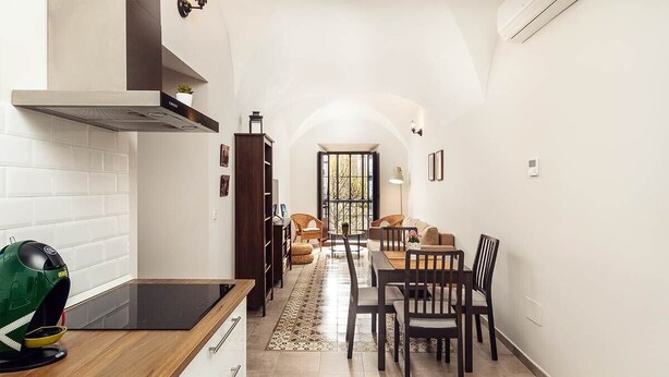 Eine schmale Küche mit modernem Herd, ein Essbereich mit Holztisch und -stühlen sowie ein Wohnzimmer mit Sofa und Couchtisch.