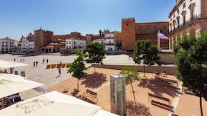 Una plaza histórica con un castillo, mesas al aire libre y cielo despejado.