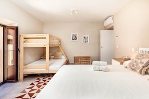 A bedroom with a bunk bed, a large bed, a wardrobe, a small table, and a wall-mounted air conditioner.