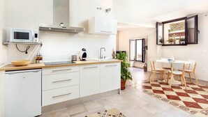 Una cocina moderna con armarios blancos, microondas y pileta. Hay un comedor con mesa y sillas.