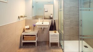 A modern bathroom with a glass shower enclosure, a sink with a mirror above it, and a small shelf with toiletries.