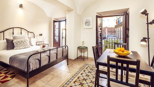 A bedroom with a bed, bedside table, lamp, and a view of the outside.