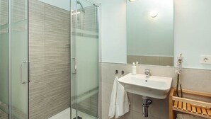 A modern bathroom with a glass shower enclosure, a white sink, and a wooden shelf.