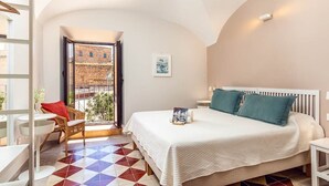 A hotel room with a bed, a small table, a chair, and a view of the outside.