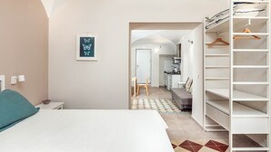 A bedroom with a bed, a wardrobe, a kitchenette, and a bathroom visible through an archway.