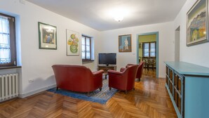 A spacious living room with a wooden herringbone floor, red leather armchairs, a flat-screen TV, and a blue cabinet. - Hladik House - Alpi Giulie Cosy Apartment (Tarvisio)