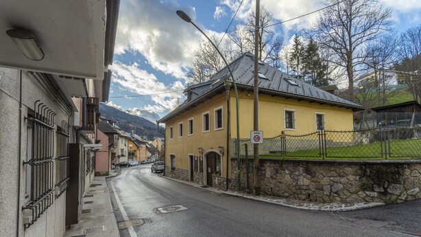 A narrow street with a yellow building, stone wall, and a fenced area. - Hladik House - Alpi Giulie Cosy Apartment (Tarvisio)