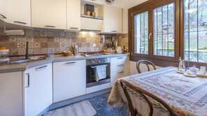 A kitchen with white cabinets, patterned backsplash, and a window with a view of a garden. - Hladik House - Alpi Giulie Cosy Apartment (Tarvisio)