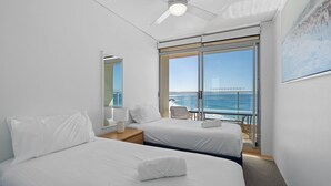 Ein Hotelzimmer mit zwei Betten, einem Balkon mit Meerblick, einem Deckenventilator und einem großen Fenster.