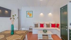A modern living room with a white sofa, a coffee table, a dining table with placemats, a vase with flowers, and a framed picture on the wall. - Maison de Pécheurs à 1mn à Pied de la Plage Cala Alcaufar (Alcaufar)