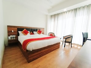 A hotel room with a large bed, wooden headboard, and a desk with chairs. - Clarks Inn Express (Samba)