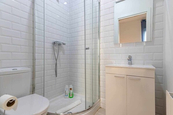 A modern bathroom with a glass-enclosed shower, a toilet, and a sink with a mirror above it.