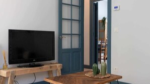 A living room with a flat-screen TV on a wooden stand, a blue door, and a cactus on a woven table. - KUIA apartment in Barakaldo, next to the metro (Barakaldo)