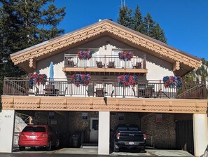 A two-story building with a stone facade, a balcony with flower baskets, and a parking area with two cars. - 1BR I Hidden Falls I Brighton Ski Resort (Salt Lake City)