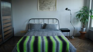 Ein Schlafzimmer mit einem Bett, einem Nachttisch, einer Stehlampe, einer Zimmerpflanze und einem Fenster.