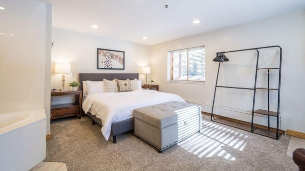 A bedroom with a bed, bedside tables, a lamp, a window, and a metal rack.