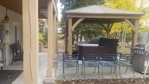 A covered patio with a hot tub, outdoor seating, and a barbecue grill.