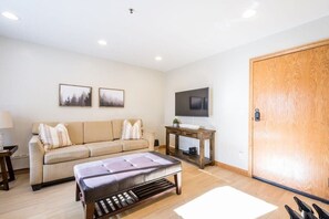 A living room with a sofa, ottoman, wooden coffee table, and a TV on a stand. - 1BR I Powderhound I Brighton Ski Resort (Brighton)