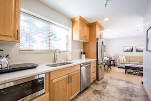 A modern kitchen with wooden cabinets, stainless steel appliances, and a window with blinds.