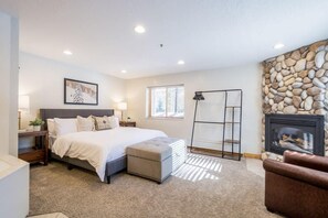 A bedroom with a bed, bedside tables, a lamp, a fireplace, and a window. - 1BR I Powderhound I Brighton Ski Resort (Brighton)