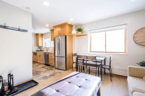 A modern kitchen with wooden cabinets, a stainless steel refrigerator, and a dining area with a table and chairs.