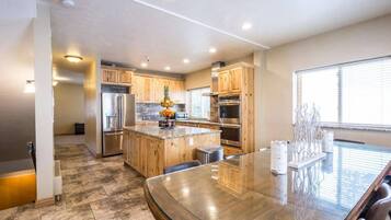 A modern kitchen with wooden cabinets, stainless steel appliances, and a glass dining table.