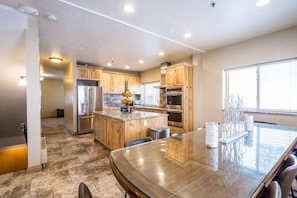 A modern kitchen with wooden cabinets, stainless steel appliances, and a glass dining table. - 5BR I Majestic l Brighton Ski Resort (Brighton)
