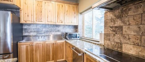 A kitchen with wooden cabinets, a stainless steel refrigerator, a microwave, and a stove.